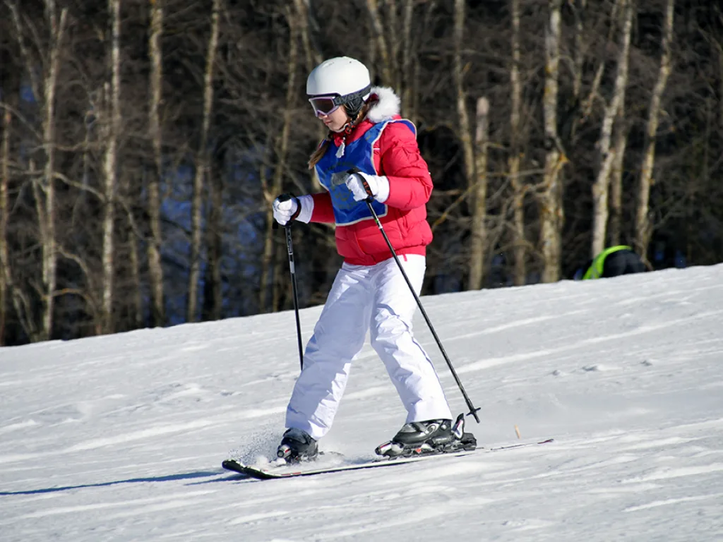 Skifahrerin in roter Jacke und weißer Hose auf der Piste.